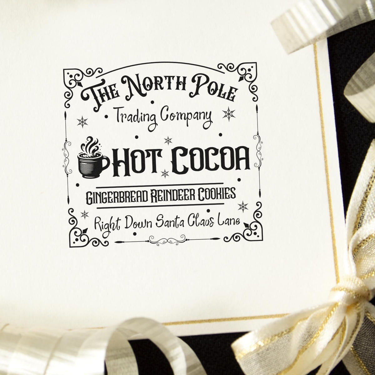 The North Pole Trading Company Hot Cocoa Compact Pre-Inked Stamp – Slim imprint stamped in black ink. An ornate rectangular sign reads "The North Pole Trading Company Hot Cocoa" with a steaming mug and gingerbread-reindeer-cookie text.