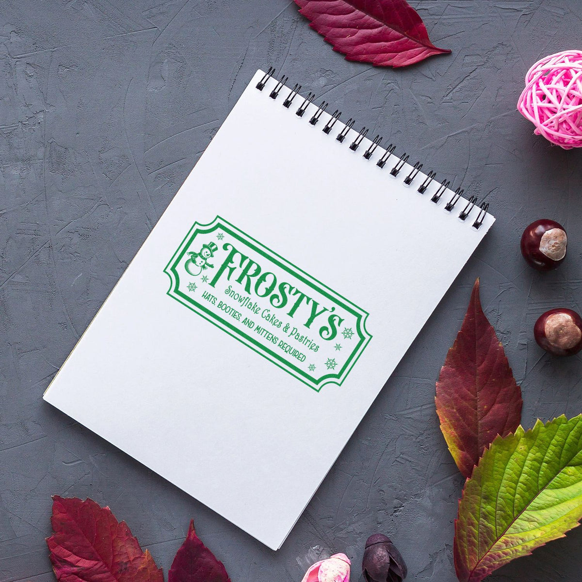 Custom rubber stamp impression on notebook for Frosty's Snowflake Cakes & Pastries holiday bakery branding.