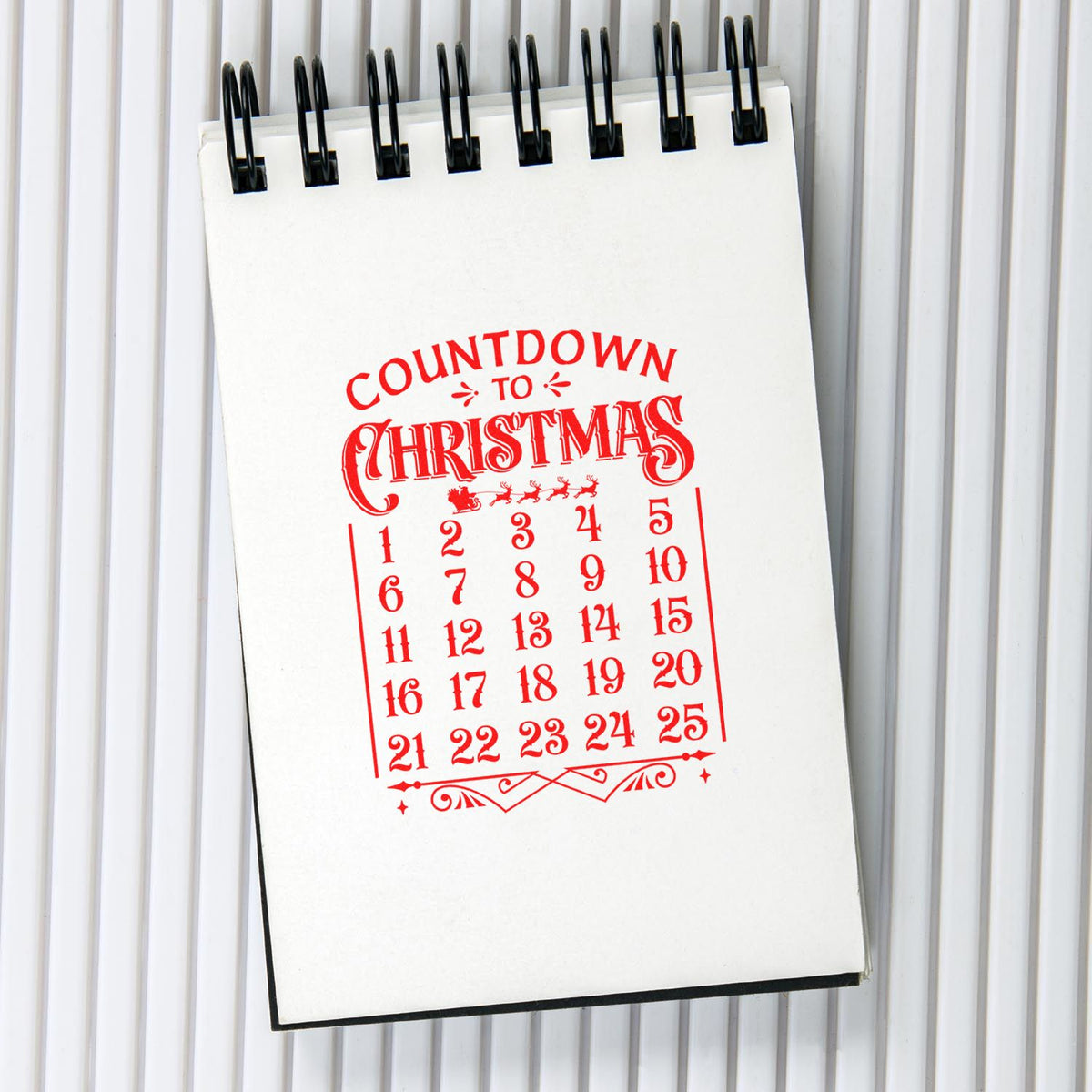 Red Christmas countdown rubber stamp on spiral notebook, featuring a numbered calendar for holiday crafts and planning.