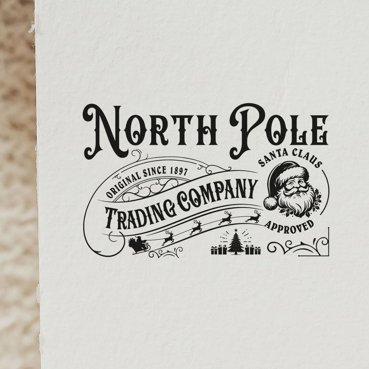 North Pole Trading Santa Approved Tree Motif Stamp - Premium Vintage Pro Wooden imprint stamped in black ink. A vintage North Pole Trading Company design includes a Santa face marked "Santa Claus approved," small trees, and sweeping scrollwork.