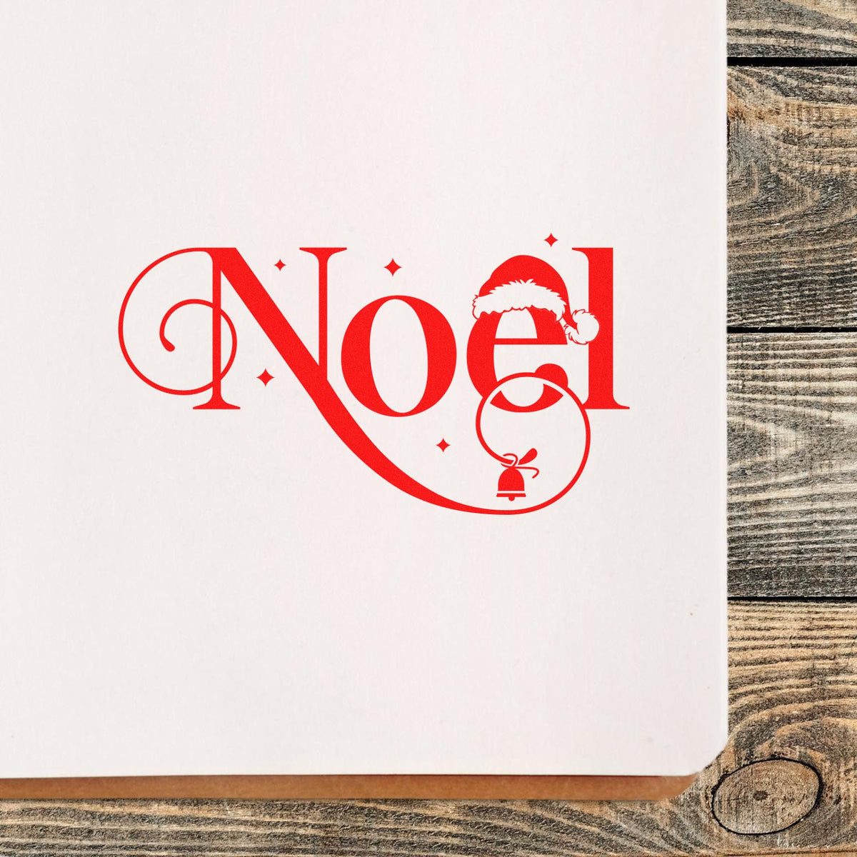 Noel Christmas rubber stamp design in red script with Santa hat and bell on white paper.
