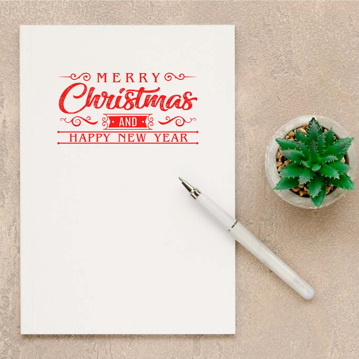 Merry Christmas and Happy New Year rubber stamp design on a blank greeting card with pen and potted plant.