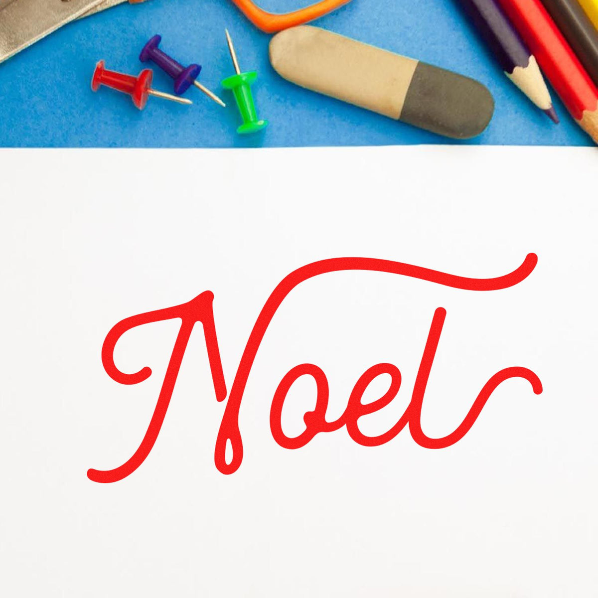 Noel holiday rubber stamp design on white paper with pencils, pins, and eraser.