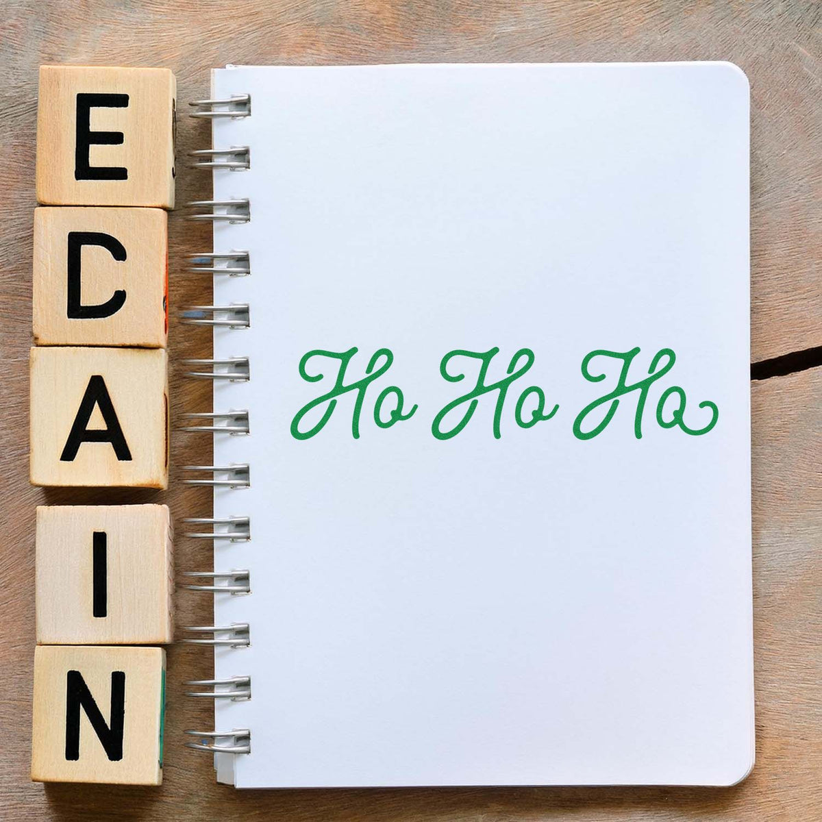 Wooden alphabet rubber stamps next to a notebook stamped with green Ho Ho Ho for holiday card making.