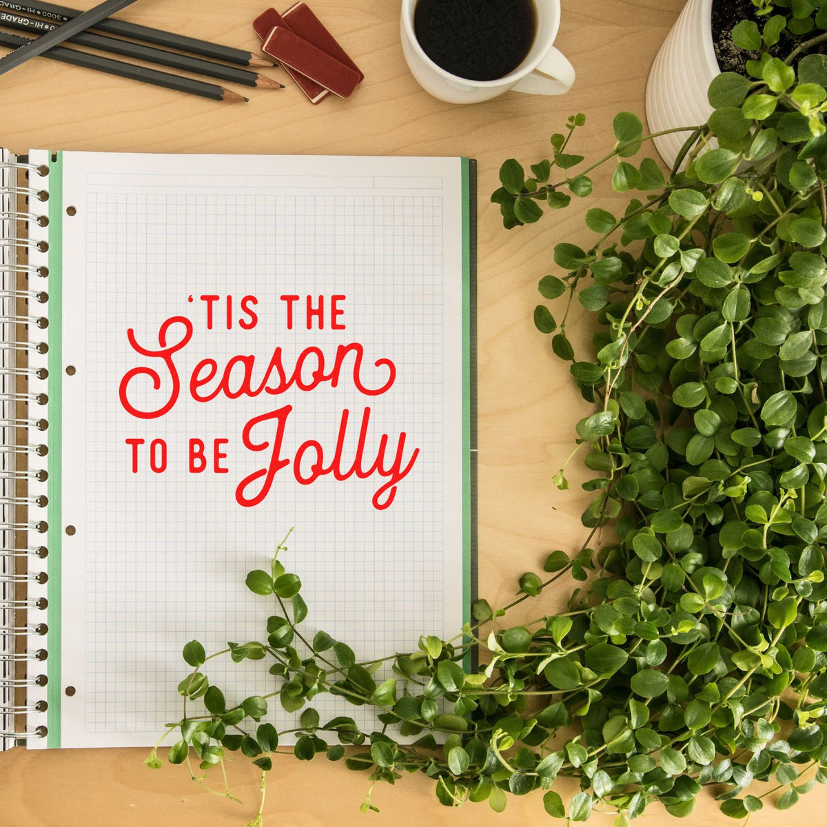 Holiday rubber stamp design with Tis the Season to Be Jolly on a notebook page, styled with greenery and desk decor.