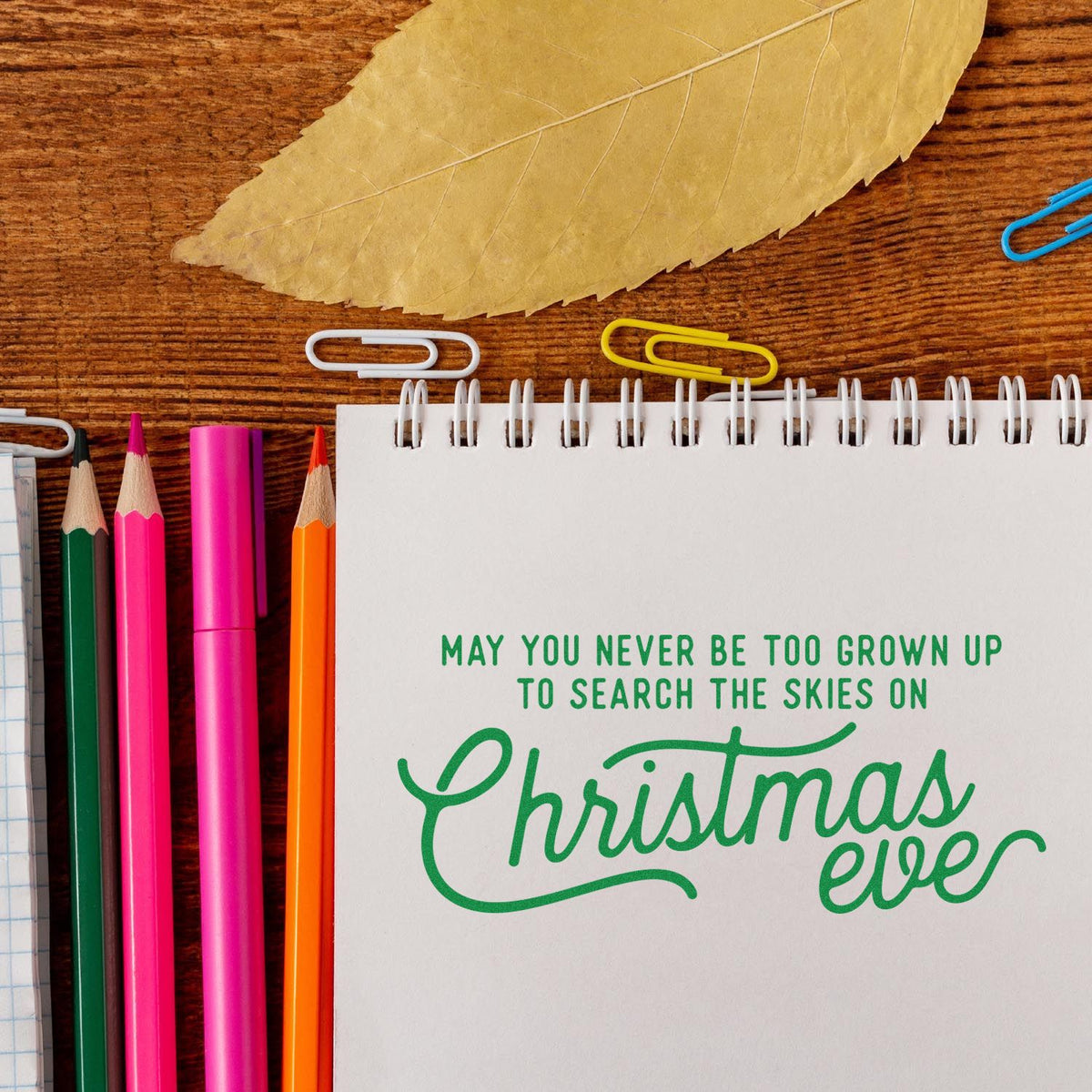 Christmas Eve rubber stamp design in notebook with green holiday quote, surrounded by pencils, paper clips, and craft supplies.