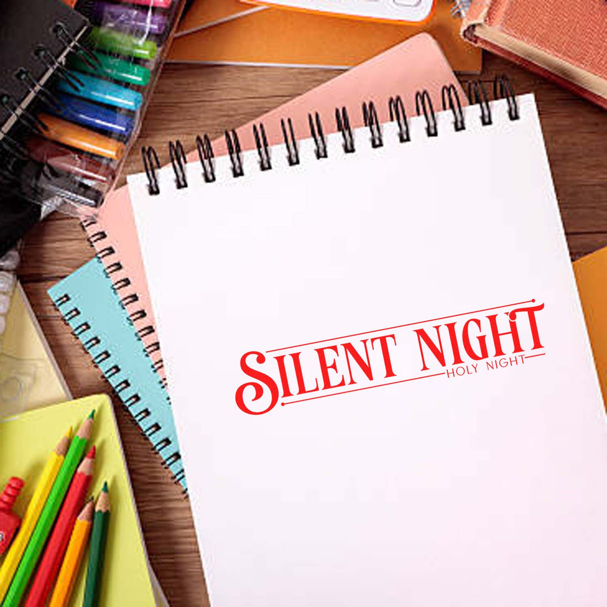 Christmas rubber stamp reading Silent Night Holy Night on a blank notebook page, with stationery and pencils around it.