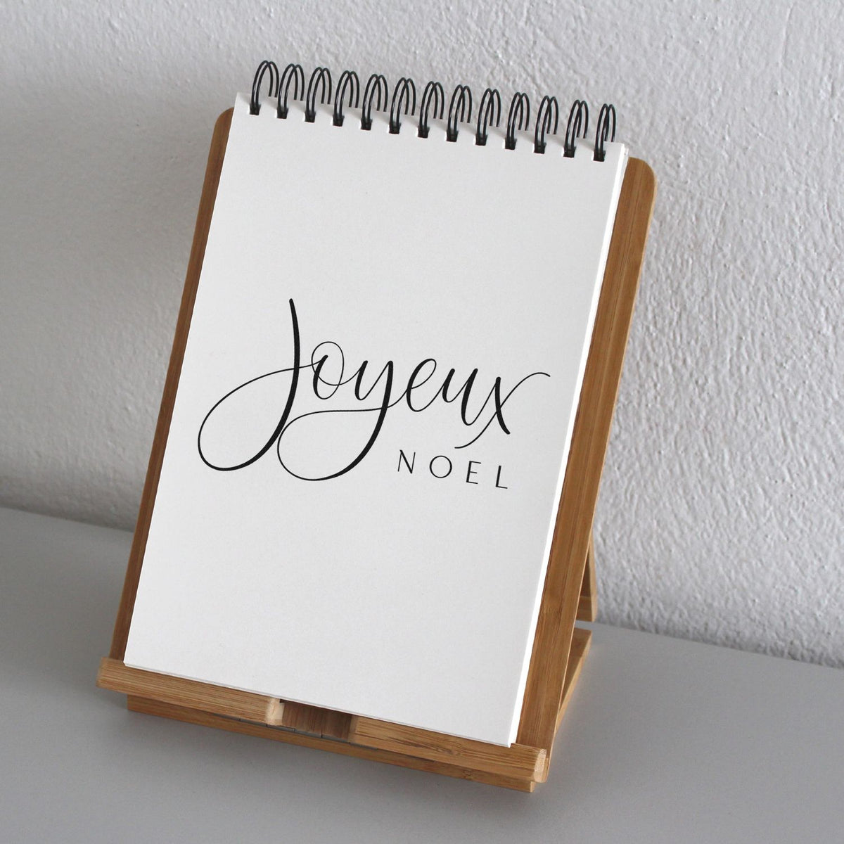 Joyeux Noel Pre-Inked Stamp – Slim imprint stamped in brown ink. The greeting "Joyeux Noel" combines a large cursive word with small widely spaced capitals.