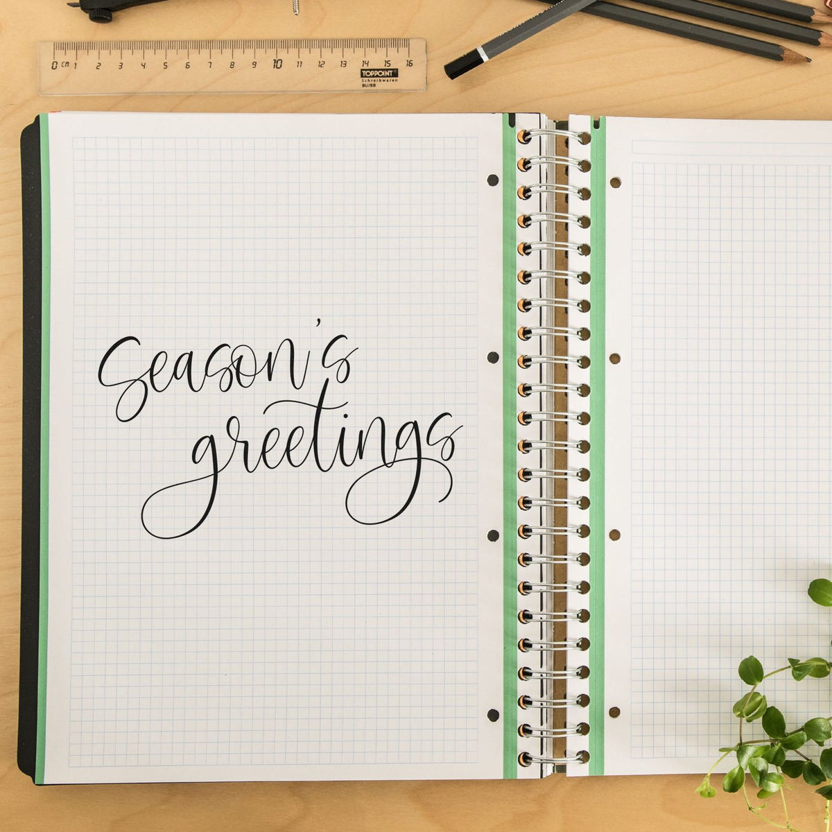 Seasons greetings calligraphy rubber stamp on a planner page, perfect for holiday card making, journaling, and craft projects.