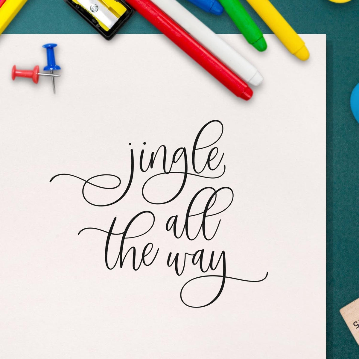 Jingle All the Way calligraphy rubber stamp on white paper, styled with colorful markers for holiday card and craft projects.