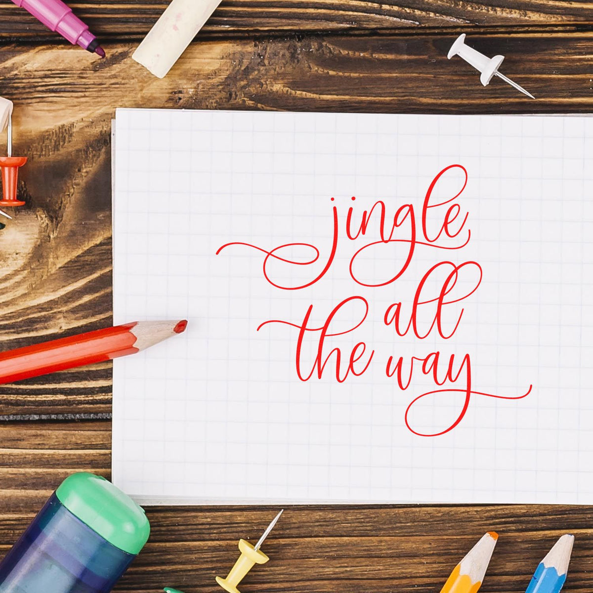 Christmas Jingle All the Way script rubber stamp design on notebook with craft supplies and pencils.