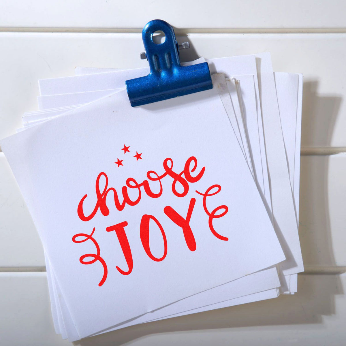 Blue binder clip holding paper stack with red Choose Joy custom rubber stamp design