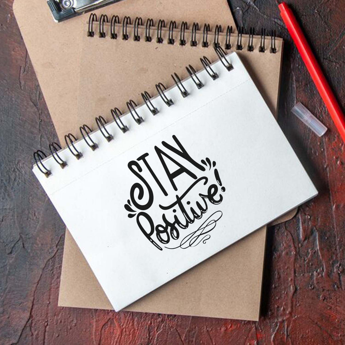 Custom rubber stamp design saying Stay Positive on a spiral notebook, perfect for motivational journaling and planners.