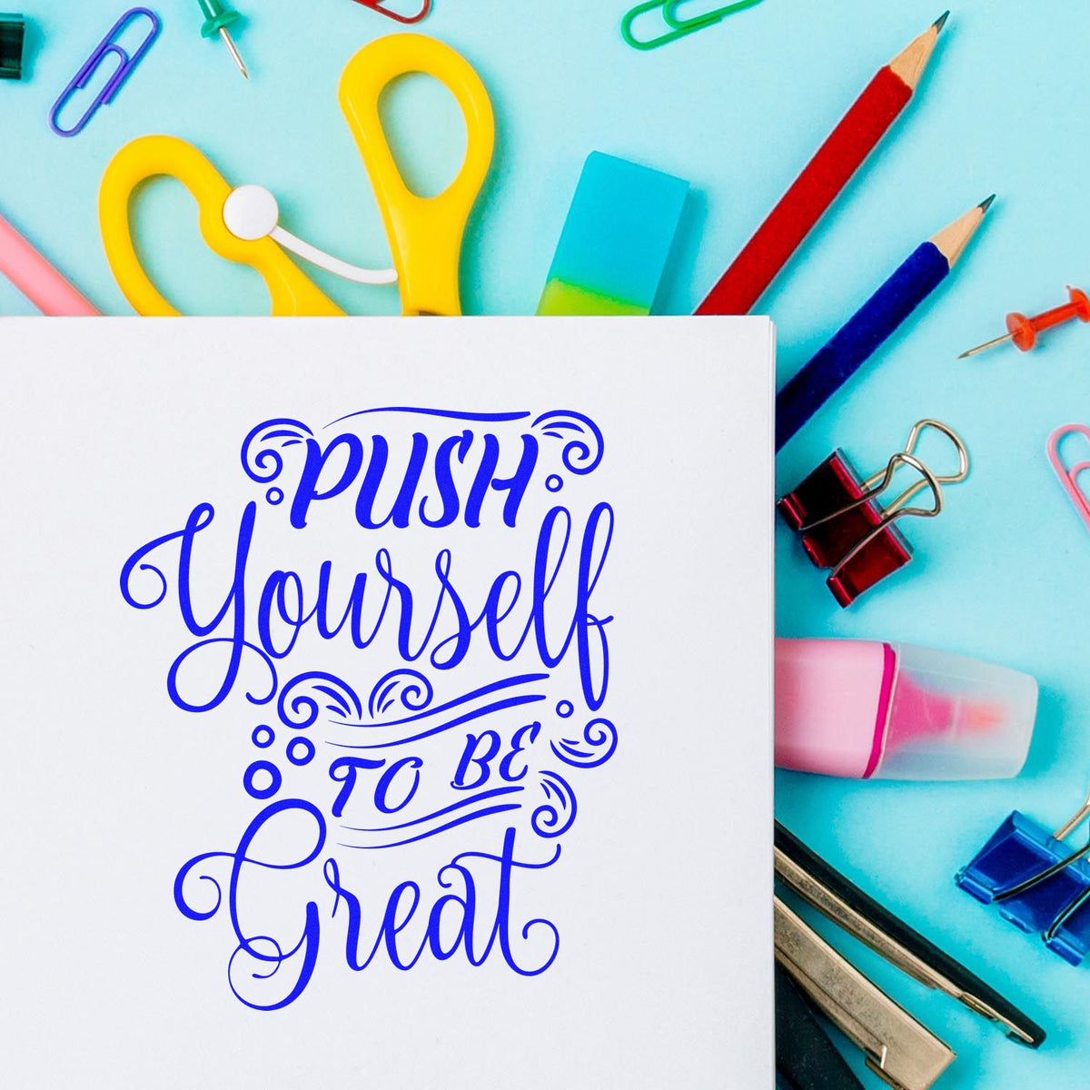 Motivational rubber stamp design reading Push Yourself to Be Great on paper, surrounded by colorful school supplies.