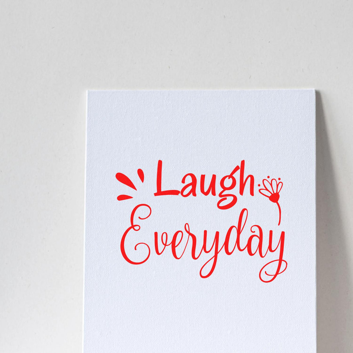 Motivational rubber stamp design reading Laugh Everyday in red script on white cardstock.