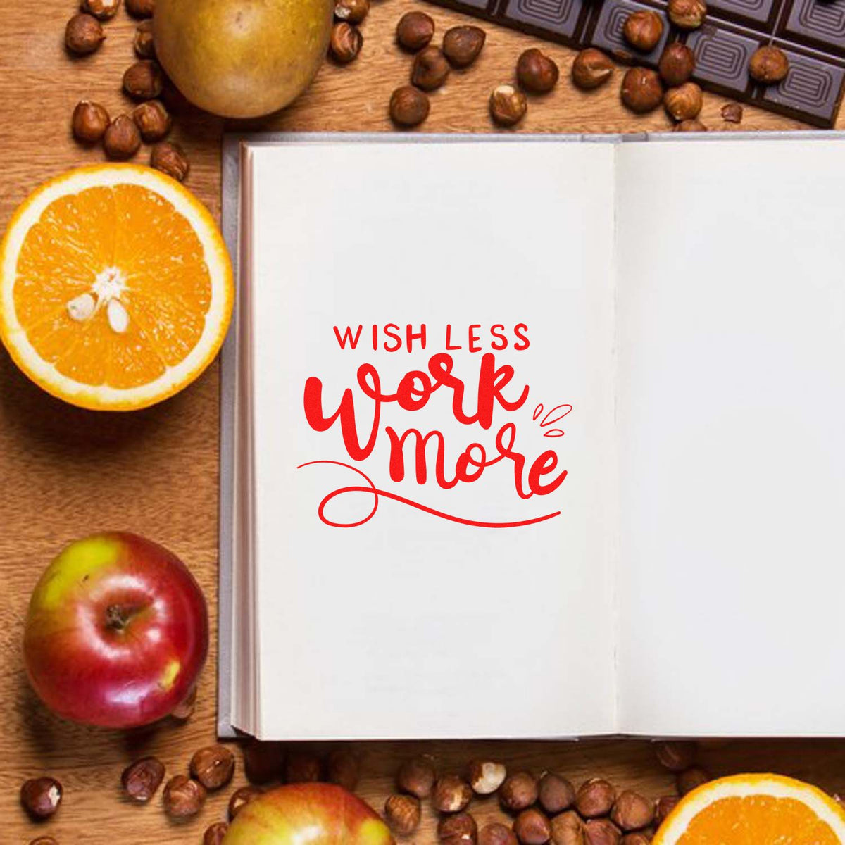 Rubber stamp mockup featuring Wish Less Work More in red on an open notebook with fruit and coffee beans.