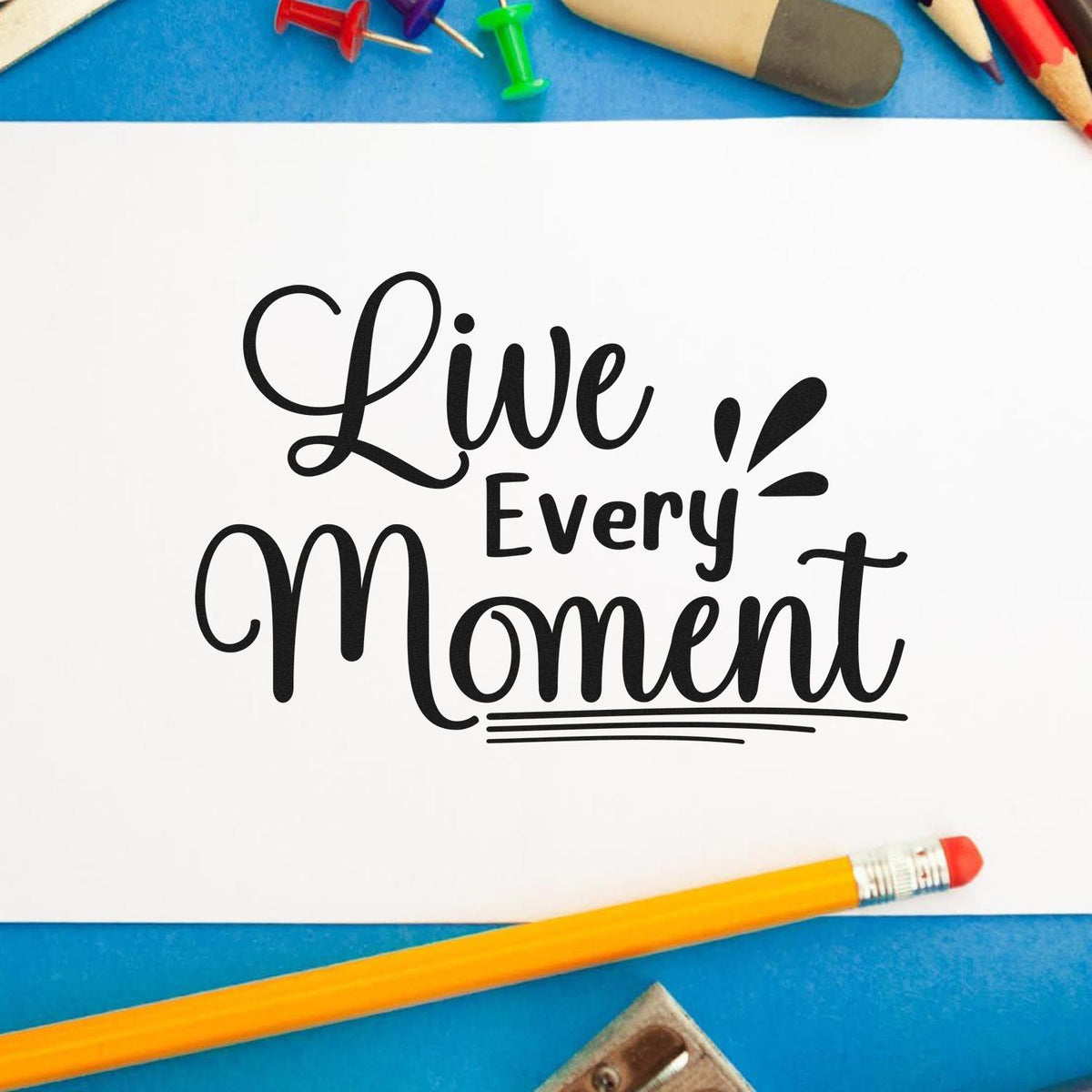 Live Every Moment rubber stamp design on white paper, surrounded by school supplies, for inspirational crafting and journaling.