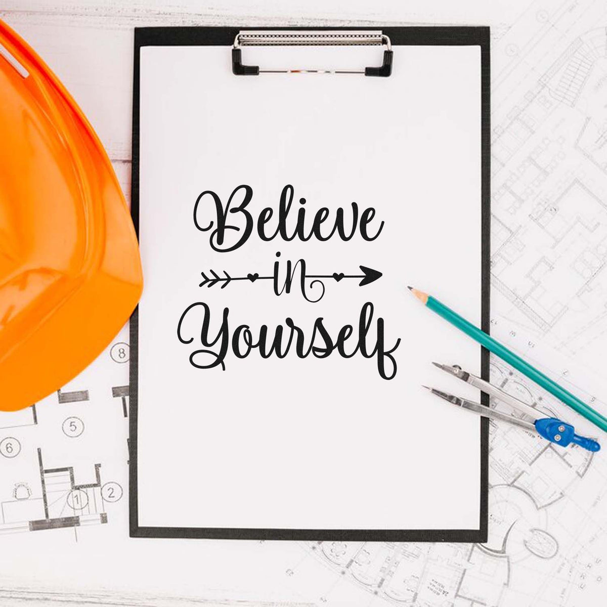 Inspirational rubber stamp design reading Believe in Yourself on clipboard with hard hat, pencils, and blueprints for builders.