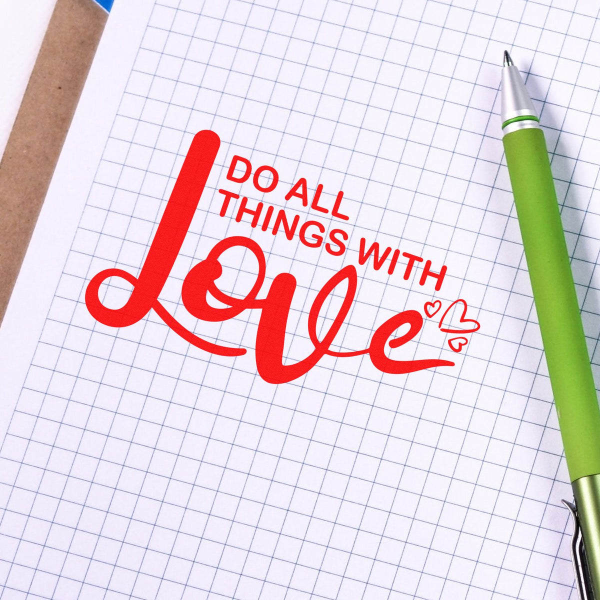 Inspirational rubber stamp design with Do All Things With Love quote on graph paper beside a green pen.