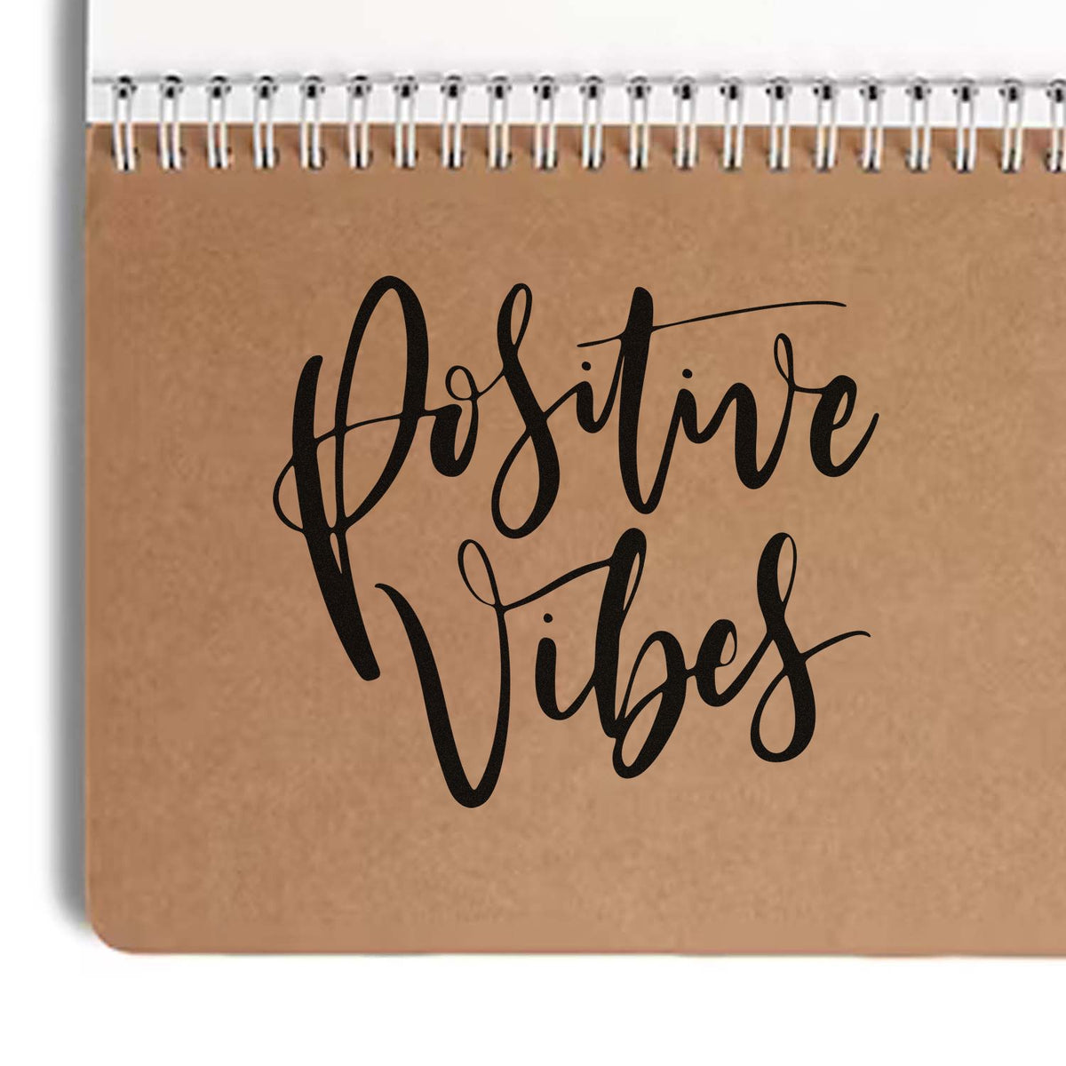 Positive Vibes rubber stamp design on kraft notebook cover, featuring bold script lettering for uplifting craft projects and branding.