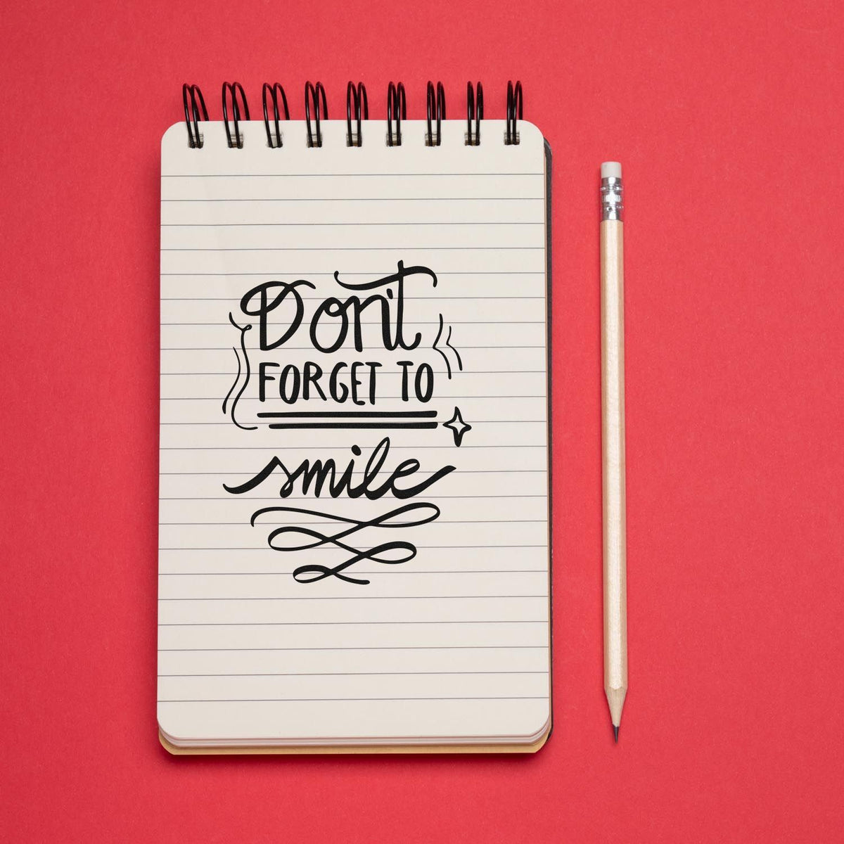 Dont Forget to Smile decorative rubber stamp design on a lined notebook with pencil on a red background