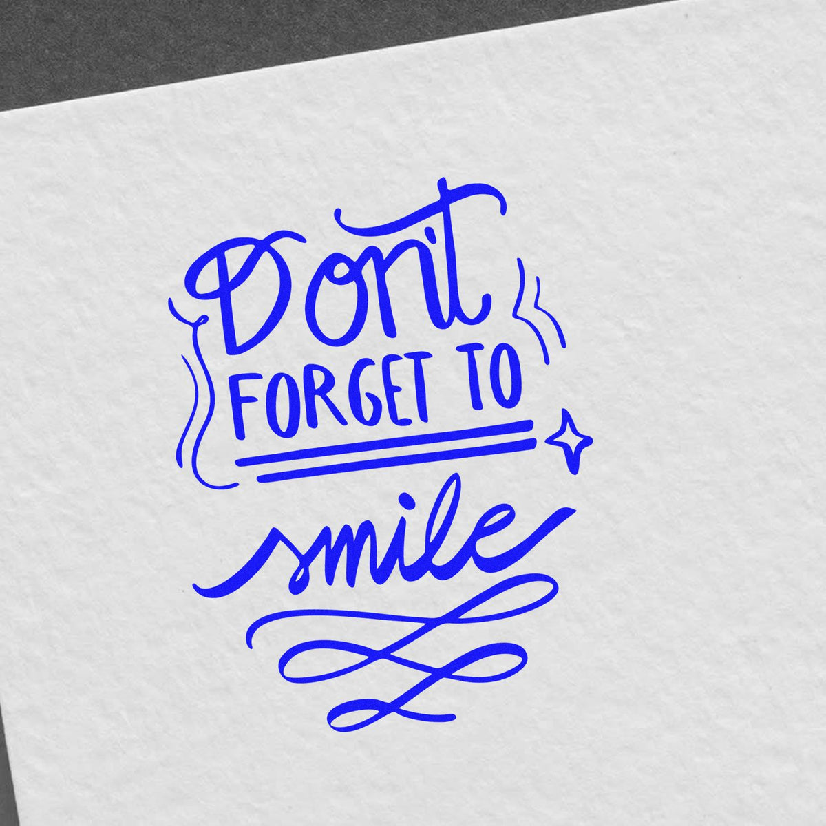 Custom rubber stamp design with the phrase Dont forget to smile in blue script on paper.