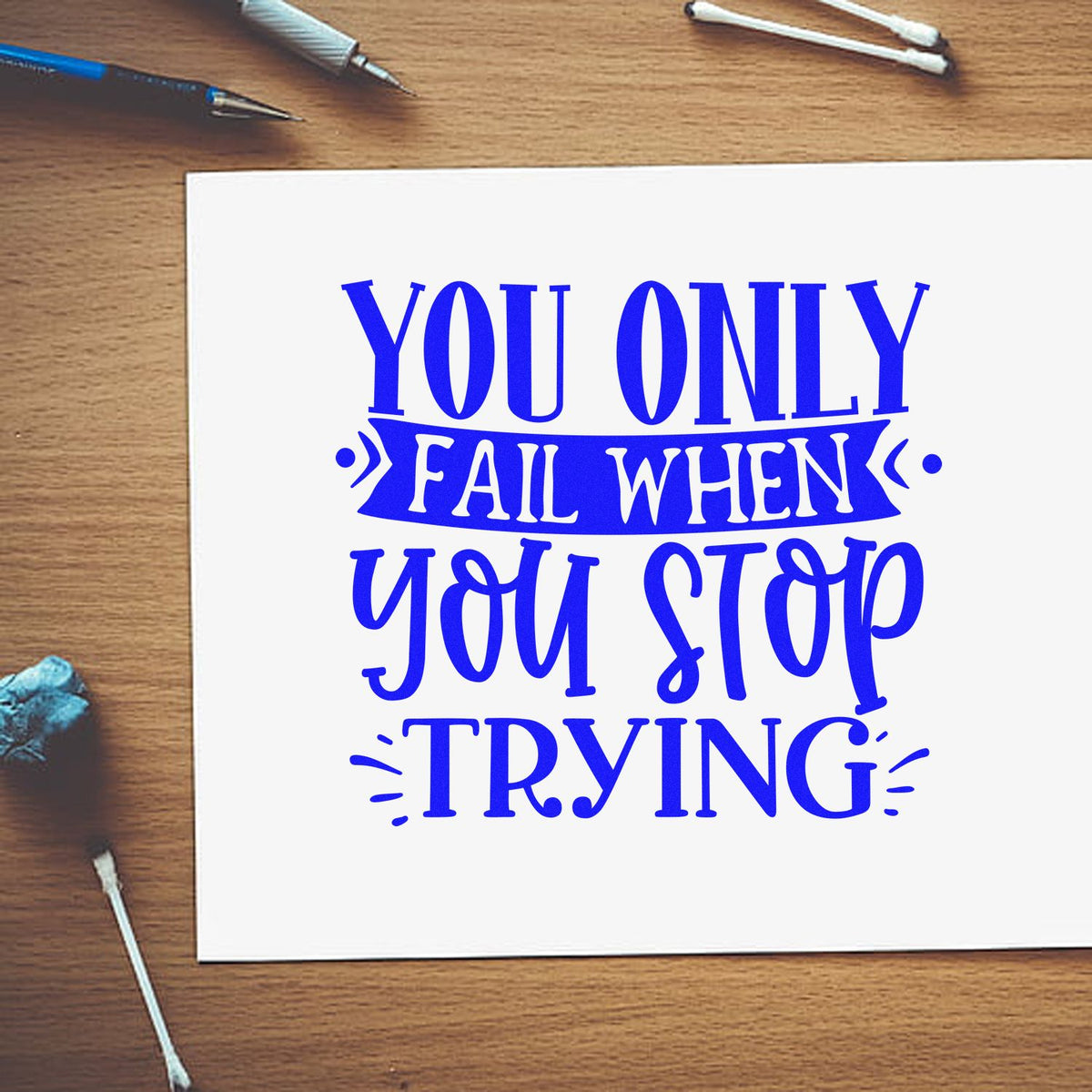 Inspirational rubber stamp quote, You only fail when you stop trying, printed in blue on white paper on a desk.