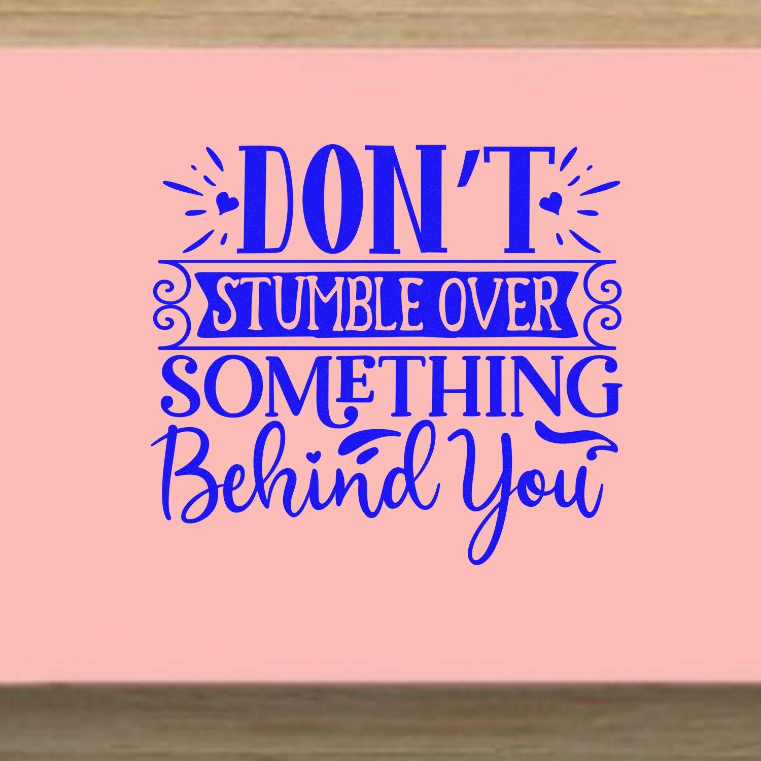 Funny inspirational rubber stamp quote: Dont stumble over something behind you in blue lettering on a pink background.