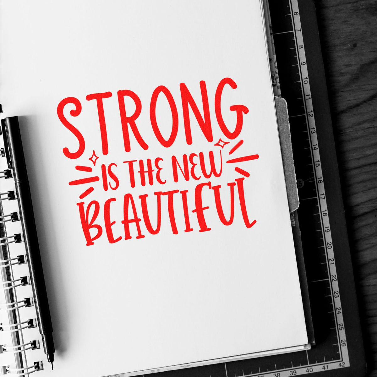 Strong Is the New Beautiful inspirational rubber stamp design in bold red lettering on a notebook page