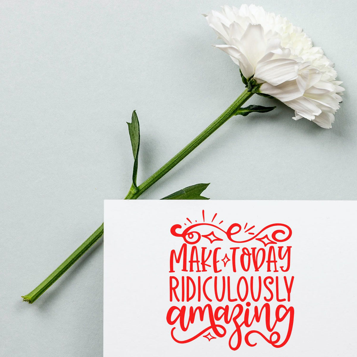 Inspirational rubber stamp with Make Today Ridiculously Amazing in red, styled with a white flower on a soft background.