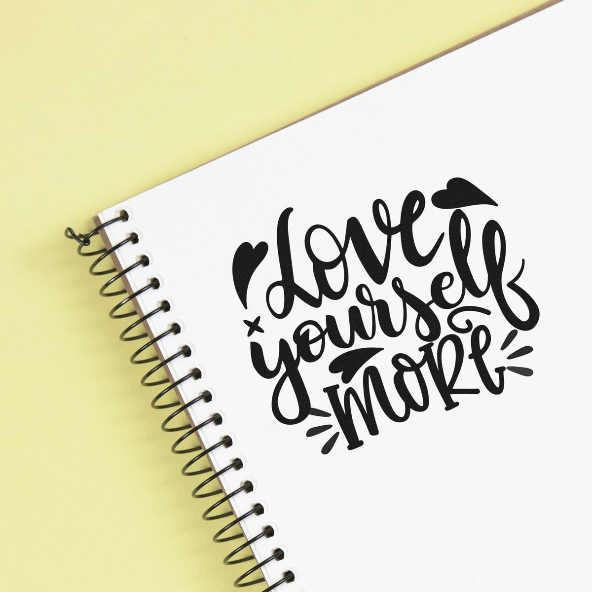 Inspirational rubber stamp design reading Love Yourself More on a spiral notebook cover.