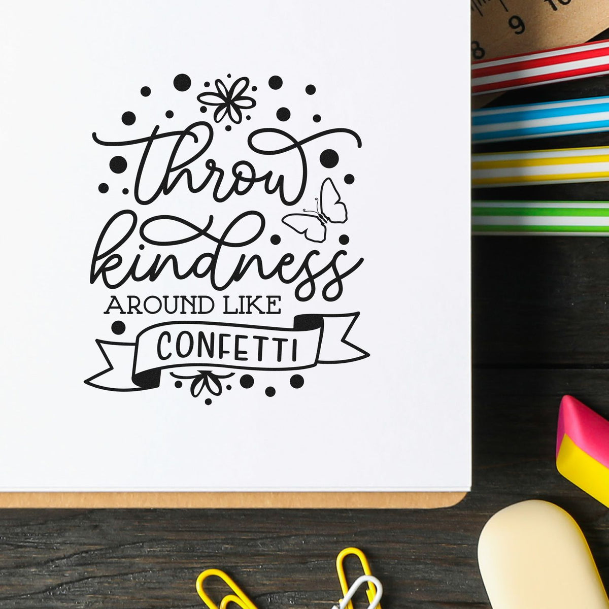 Throw kindness around like confetti rubber stamp design on white paper, with ink pads and craft supplies nearby.