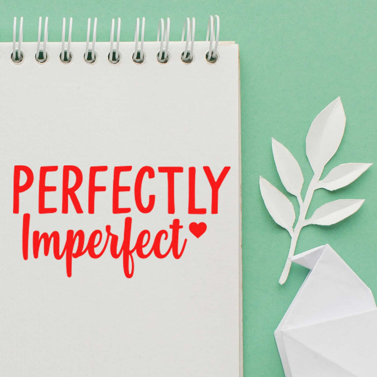 Perfectly Imperfect rubber stamp design in red on a notebook page, with paper leaves and origami on a mint green background.