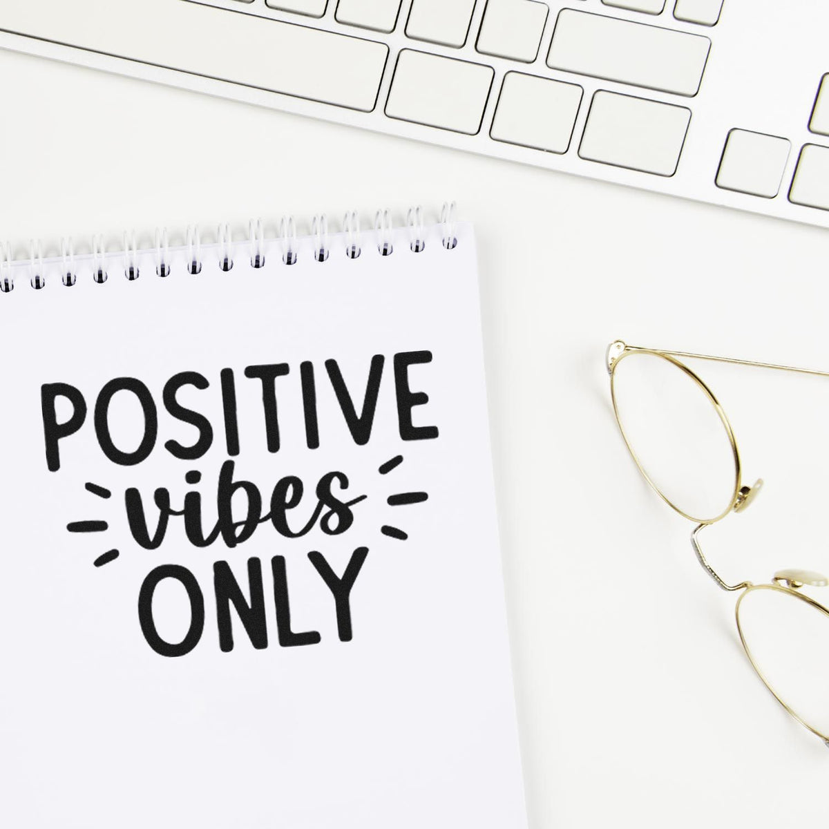 Positive vibes only rubber stamp design on notebook for motivational office decor and branding, with keyboard and glasses.