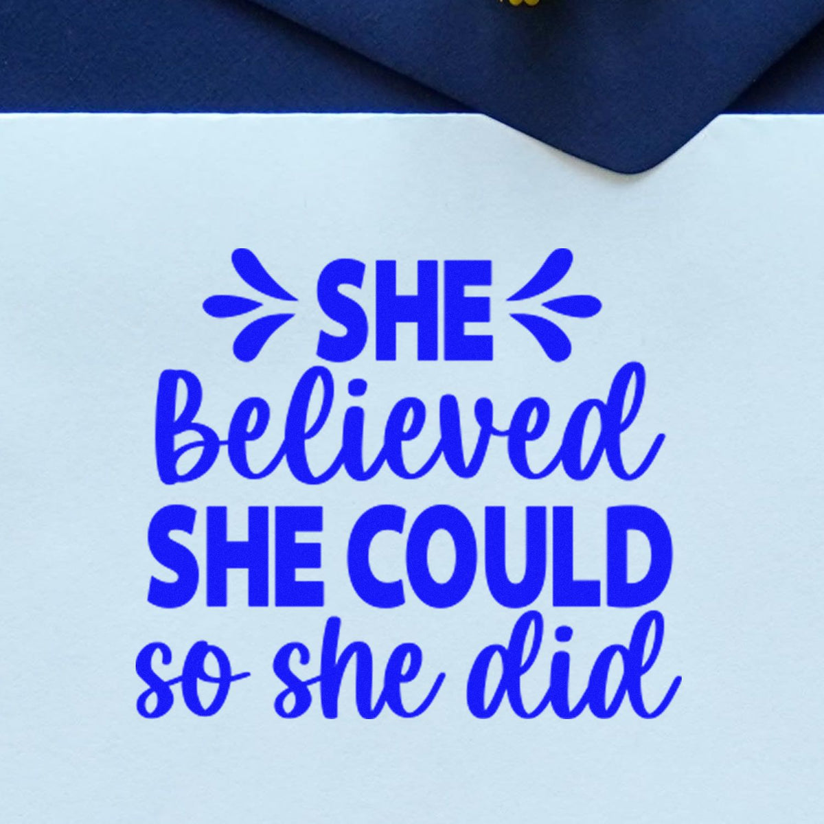 Blue motivational rubber stamp quote reading She believed she could so she did in bold blue lettering.