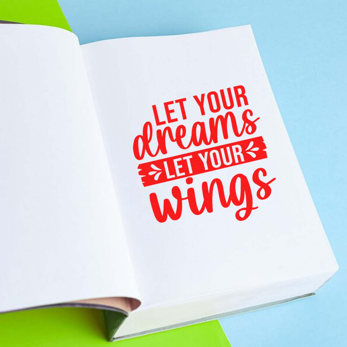 Motivational custom rubber stamp imprint with red Let your dreams let your wings quote on an open notebook page.