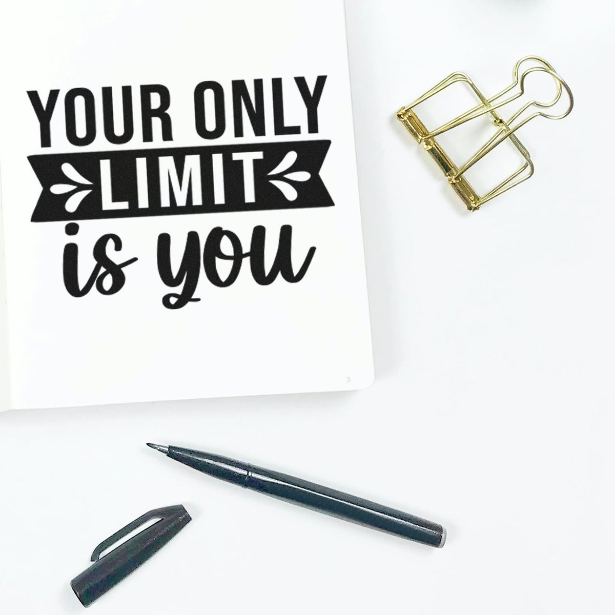 Custom motivational rubber stamp with Your Only Limit Is You quote on notebook, styled with pen and binder clip.