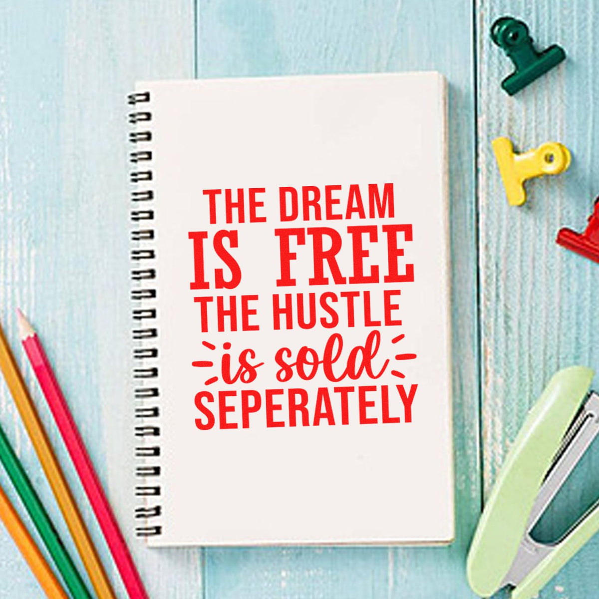 Motivational rubber stamp design on a spiral notebook reading The dream is free, the hustle is sold separately.