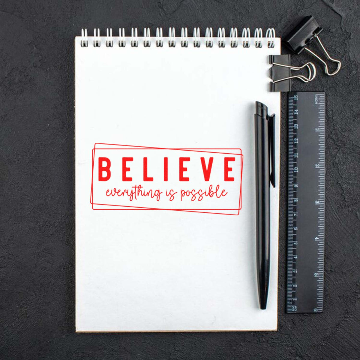 Motivational rubber stamp design with red BELIEVE everything is possible imprint on a notebook, ideal for crafts and branding.