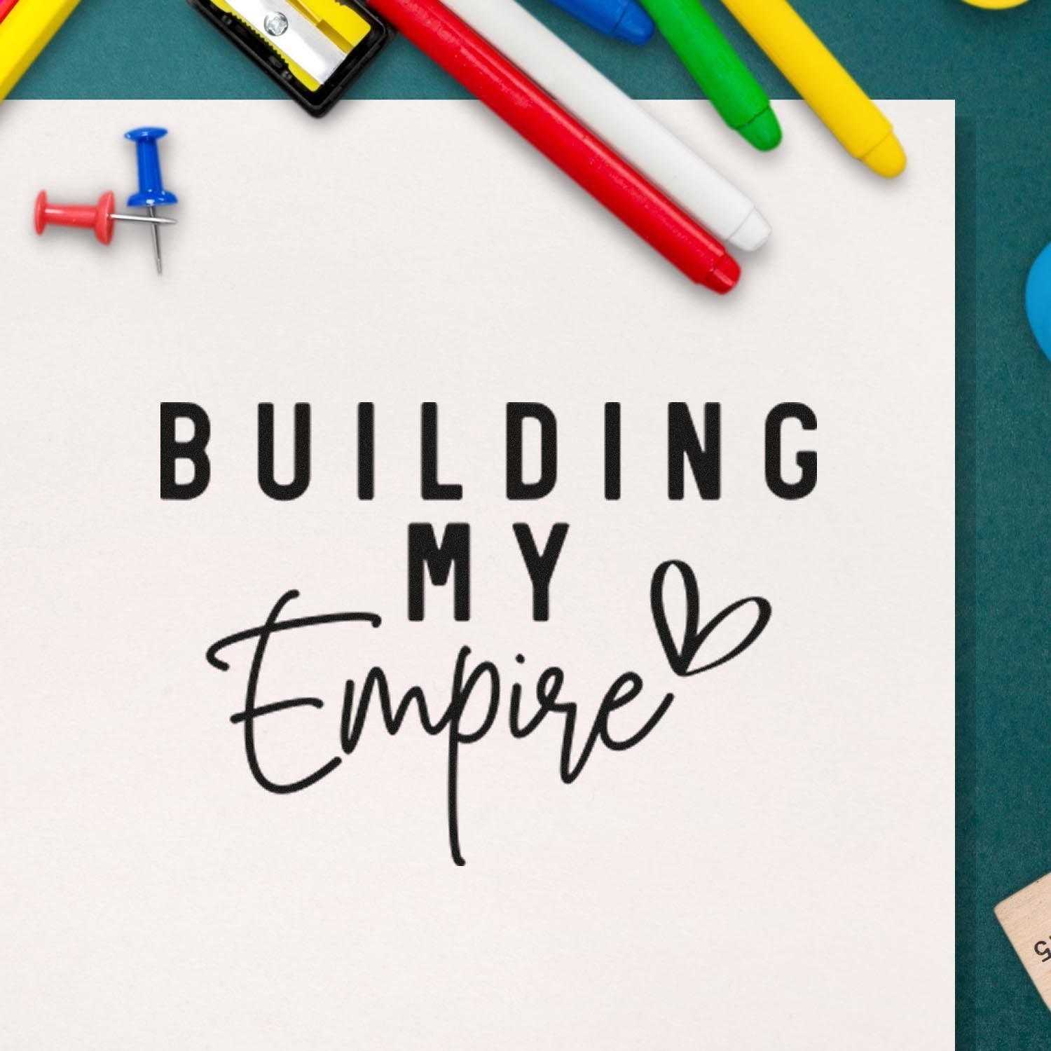 Rubber stamp design reading Building My Empire with colorful pens and push pins on a craft desk.