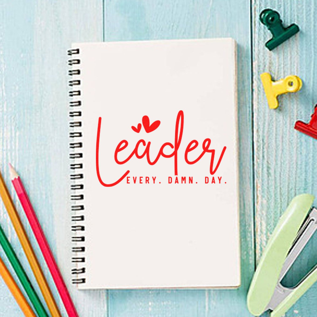 Custom rubber stamp design reading Leader every damn day on a spiral notebook with colorful stationery.