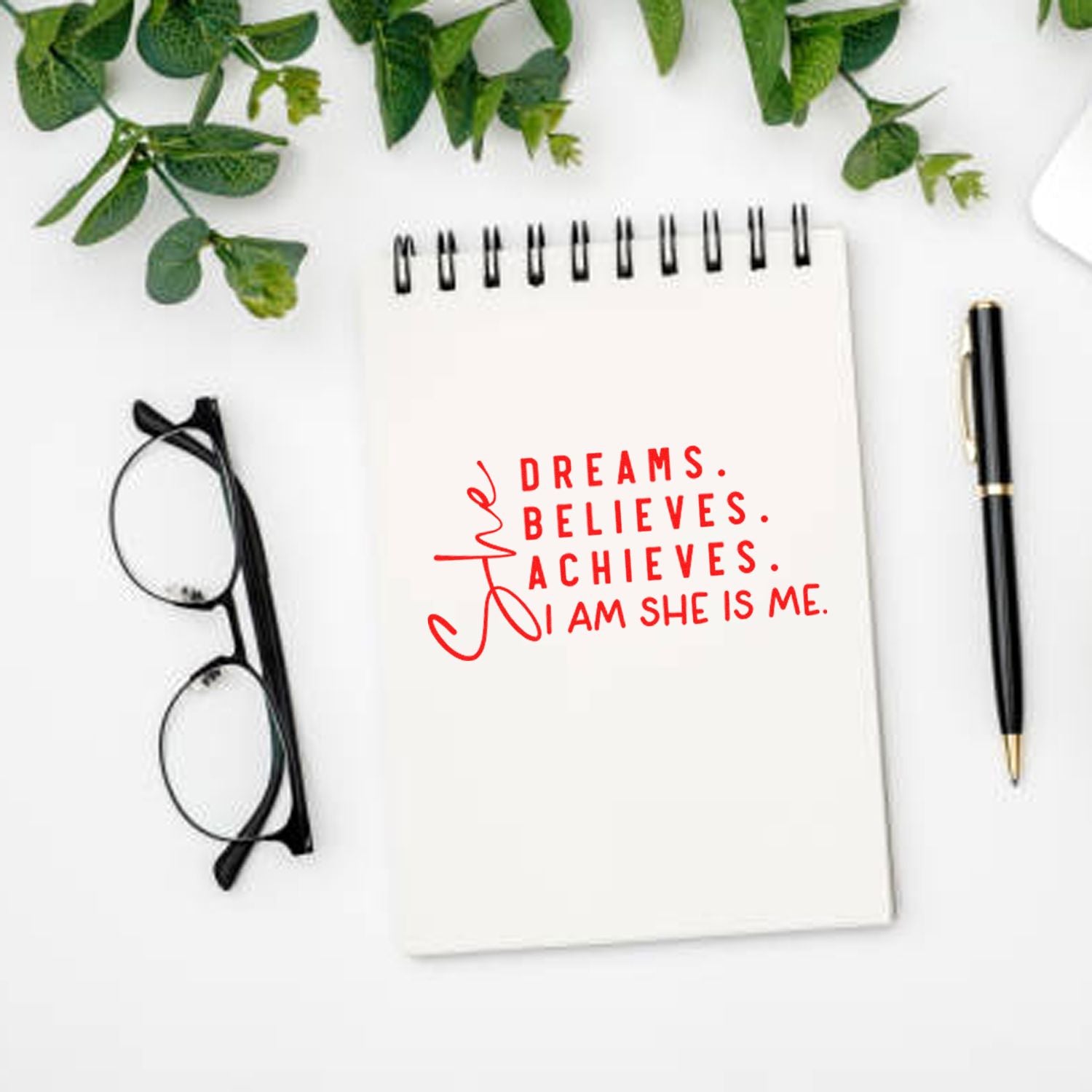 Inspirational rubber stamp on notebook with red quote, She dreams, believes, achieves. I am she is me.