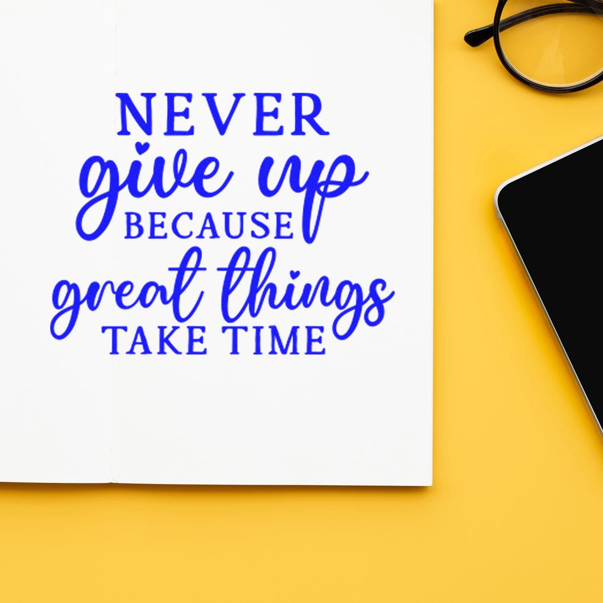 Blue inspirational rubber stamp quote, Never give up because great things take time, on notebook beside glasses and phone.