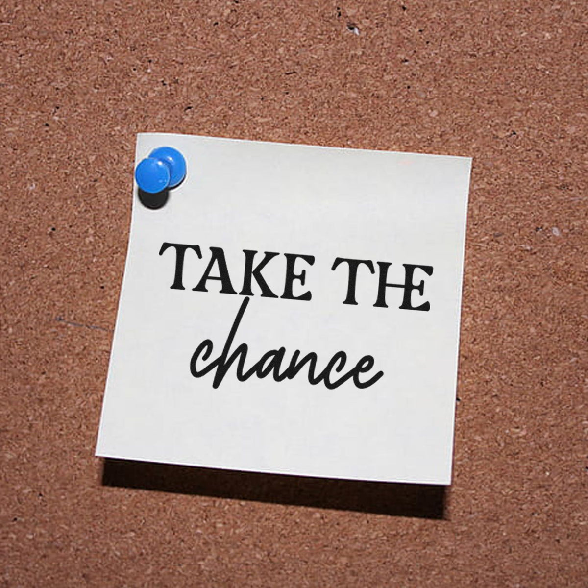 Motivational rubber stamp design reading Take the Chance pinned on a corkboard.