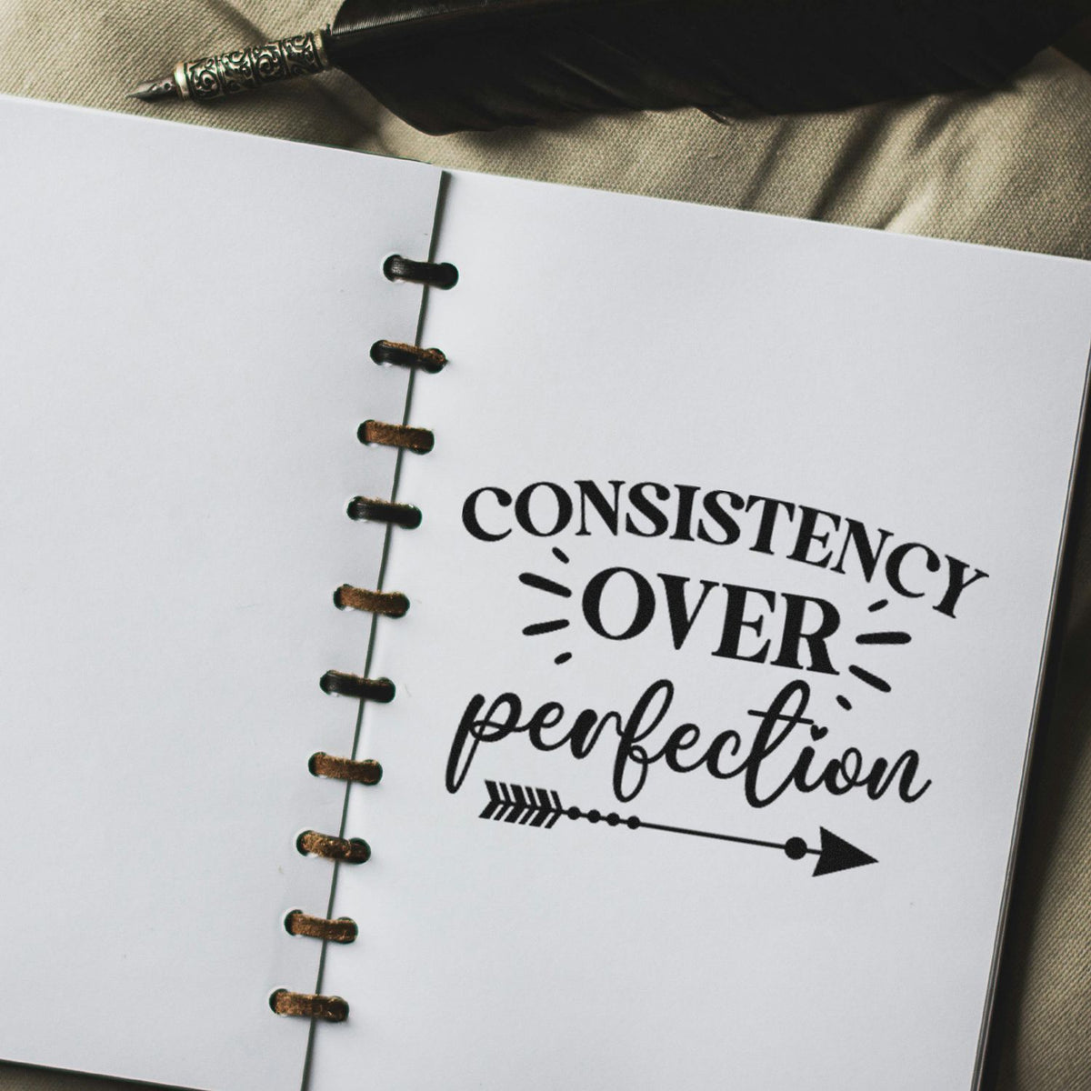 Consistency Over Perfection Arrow Slim Pre-Inked Stamp imprint stamped in black ink. The phrase "Consistency over perfection" appears with rays and a right-pointing arrow with small dot accents.