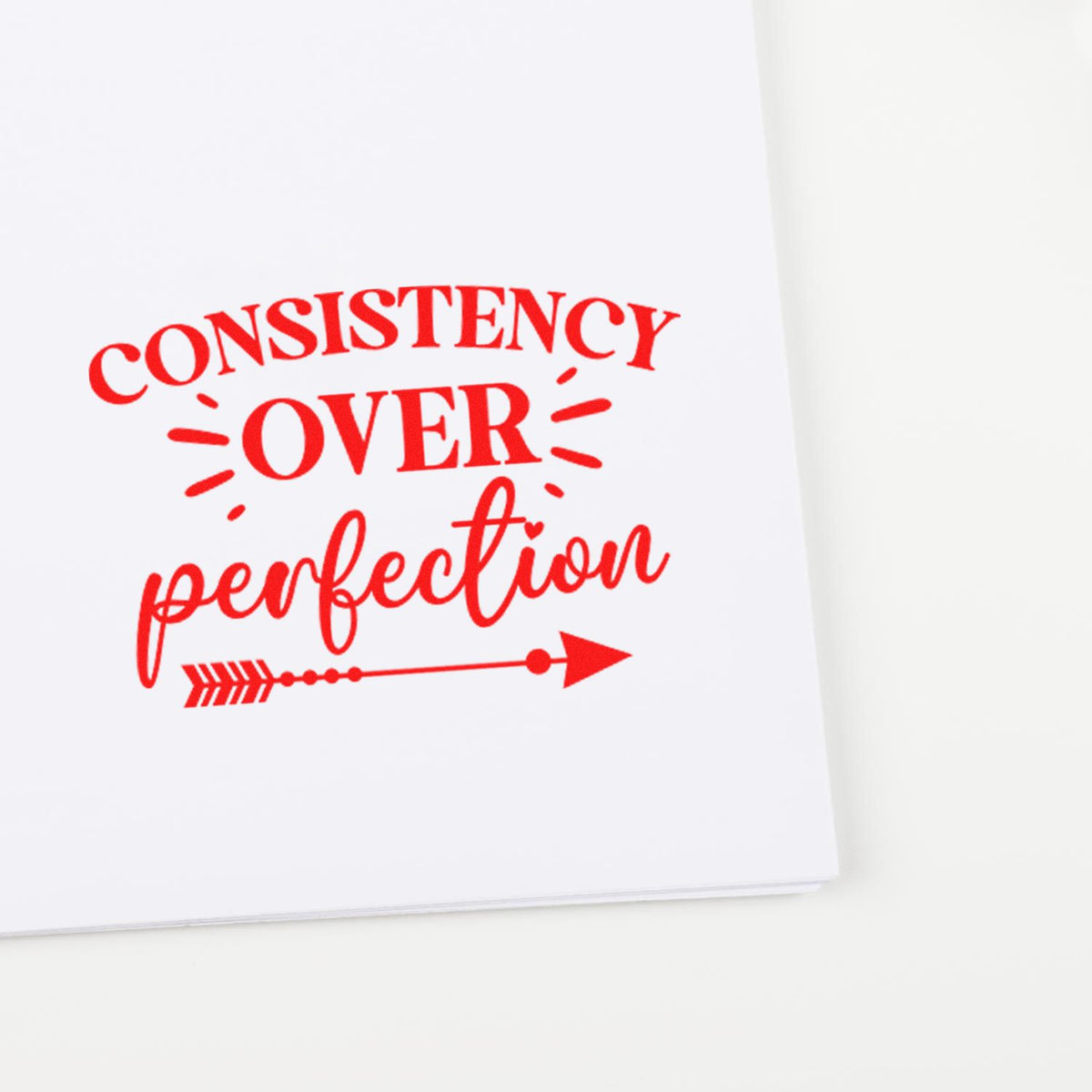 Red rubber stamp reading Consistency Over Perfection on white paper, ideal for motivational planner and craft projects.