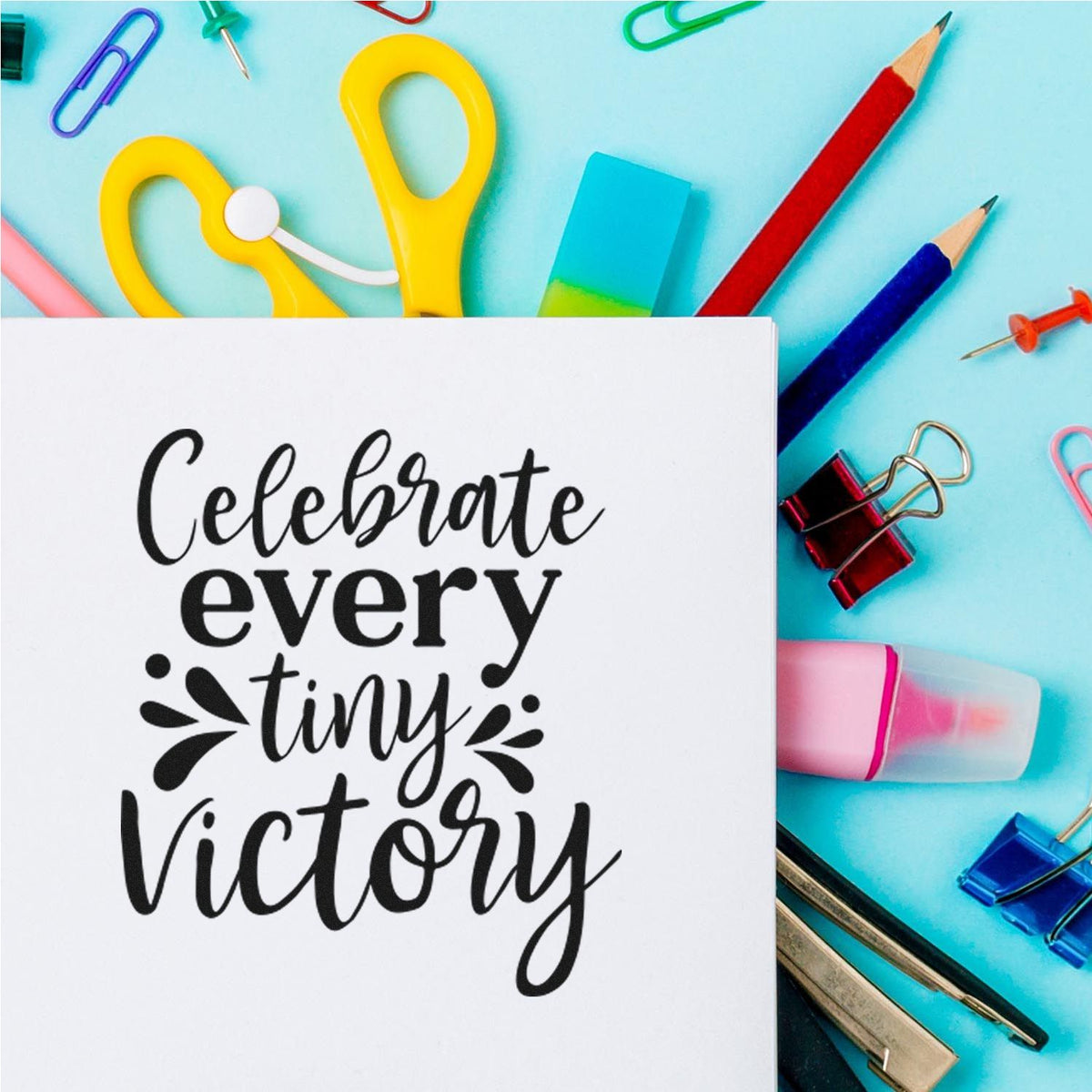 Motivational rubber stamp reading Celebrate every tiny victory on a colorful stationery background.
