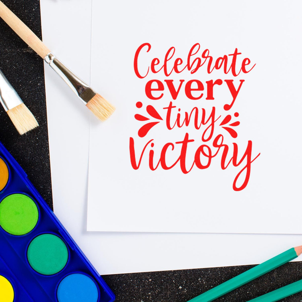 Motivational rubber stamp design reading Celebrate every tiny Victory with paint brushes and watercolor palette.