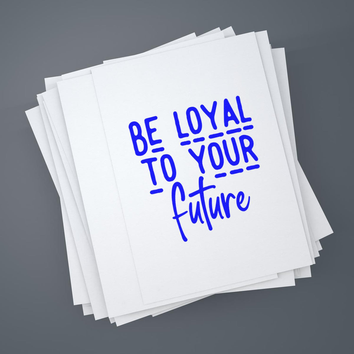 Inspirational rubber stamp design reading Be loyal to your future stamped in blue on stacked white paper.