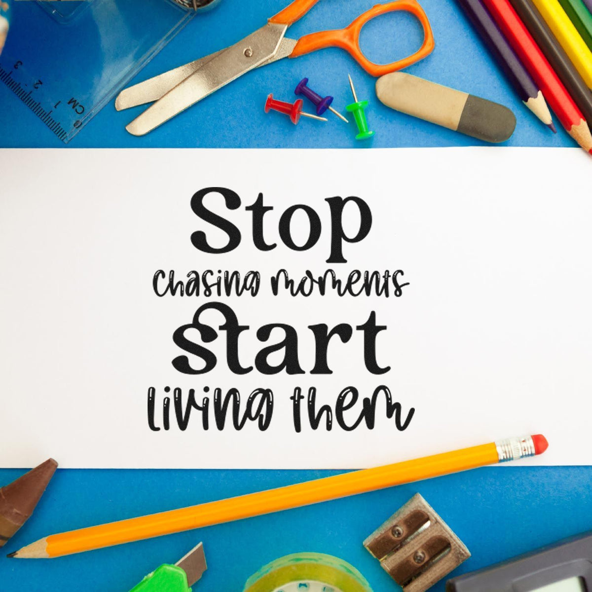 Inspirational rubber stamp quote reading Stop chasing moments, start living them on white paper with school supplies.